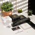 Elegante UNIQAL Schmuckverpackungen in Schwarz und Weiß mit goldenen Logos, präsentiert auf einem Tisch mit Pflanzen im Hintergrund